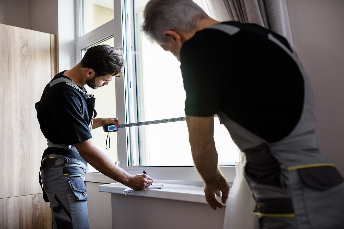 Two workers using tape to measure windows
