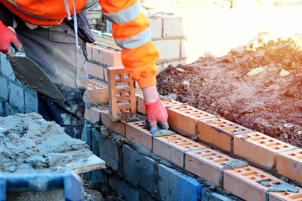 Bricklayer applying mortar and laying bricks on a building site