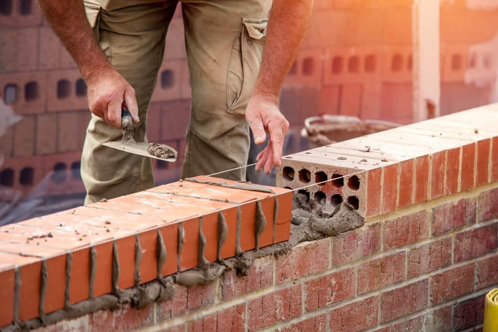 Bricklayer finishing the top course of a red brick wall with string line and trowel