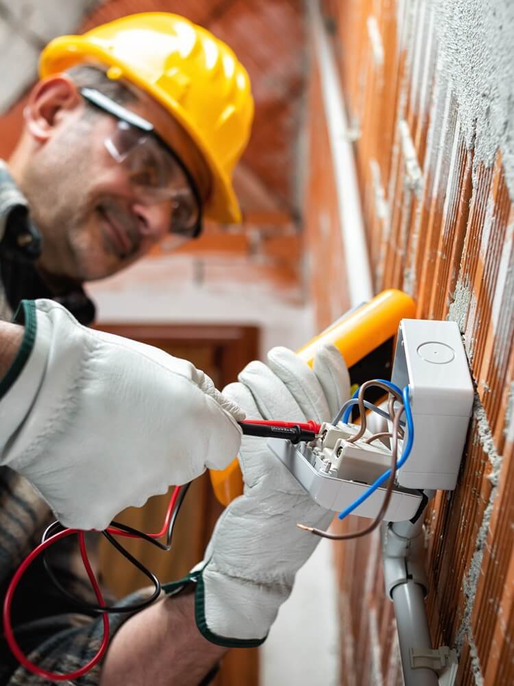 Electrician testing a wall-mounted socket with a multimeter during residential installation work.