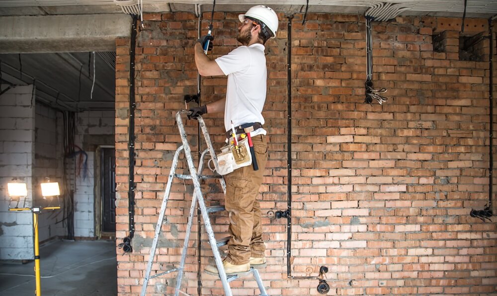 Electrician on ladder wiring an internal wall during a building fit-out project.
