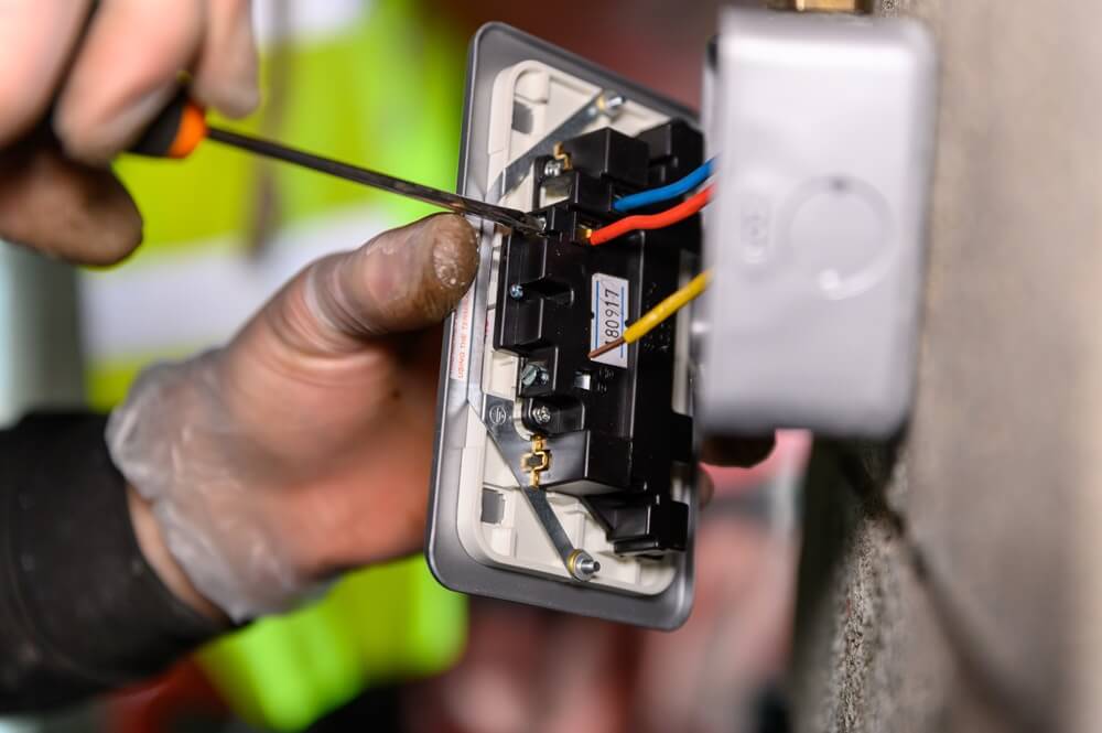 Electrician wiring a heavy-duty socket on a concrete wall using insulated tools and coloured cables.