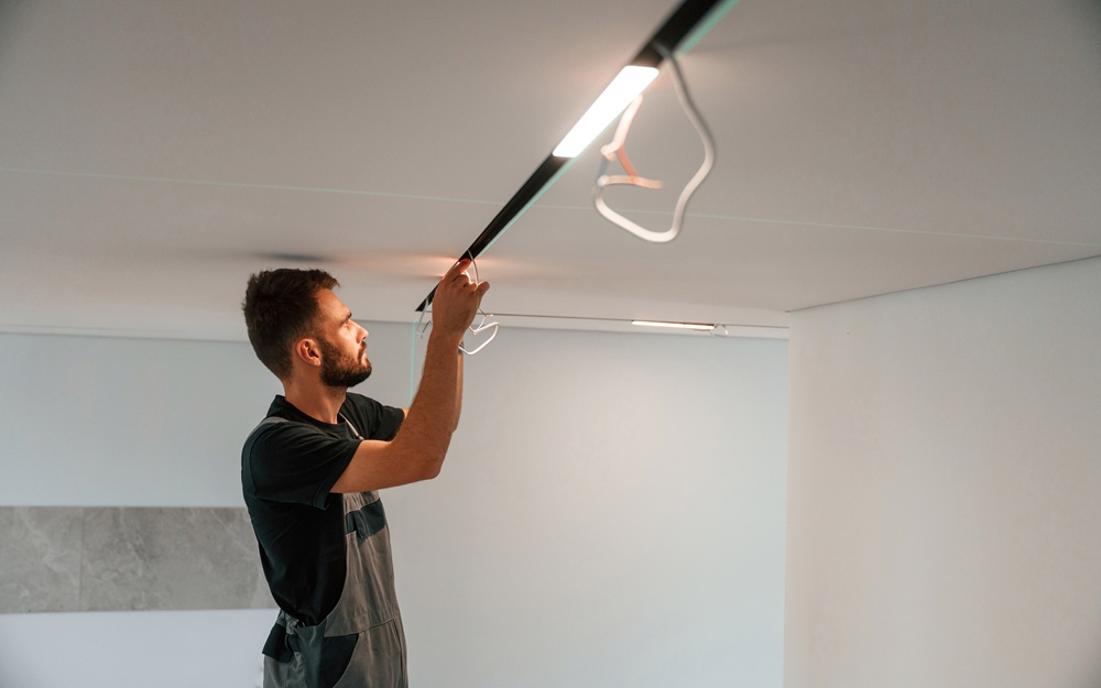 Electrician installing a suspended LED light fixture into a white ceiling during a domestic lighting upgrade.