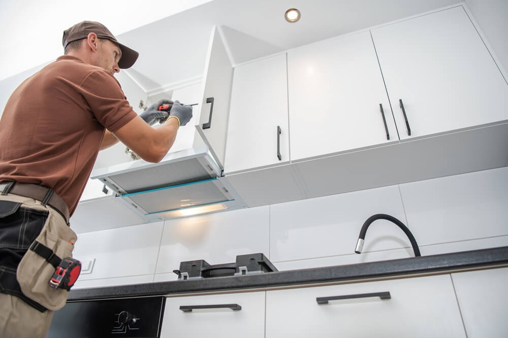 Contractor fitting white kitchen wall cabinets with a screwdriver.