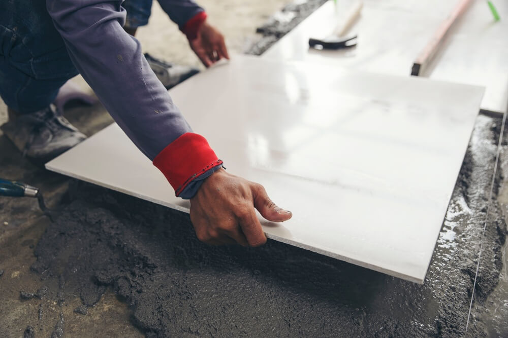 Tradesperson laying a large white ceramic tile onto floor adhesive with precision.