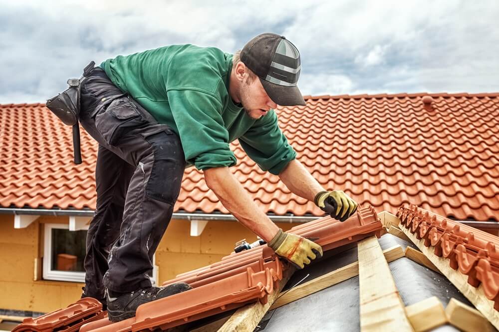 Roofer installing red clay tiles on a pitched roof with wooden battens underneath
