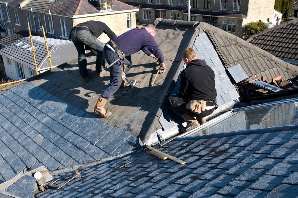 Three roofers working together on a complex pitched slate roof in a residential area