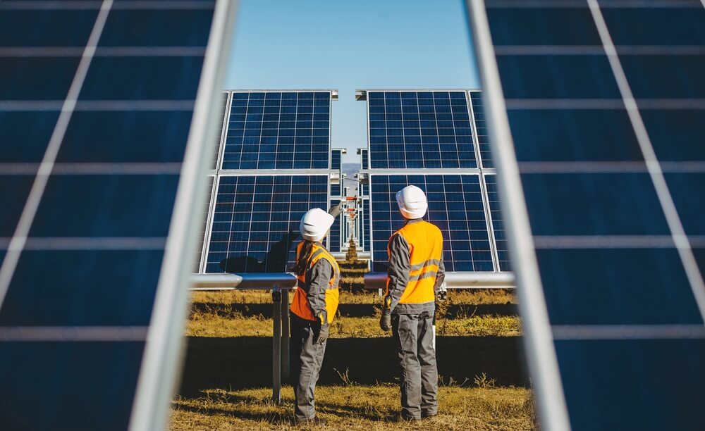 Two engineers inspecting commercial solar panel field installation between ground-mounted PV systems.