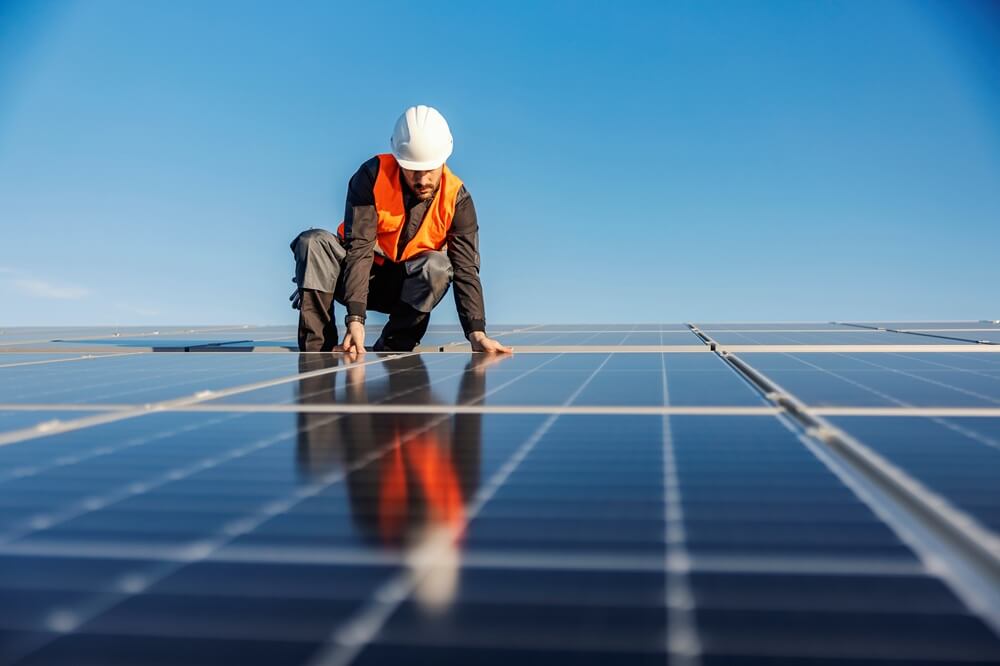 Installer in safety gear inspecting solar panels on a large commercial rooftop.