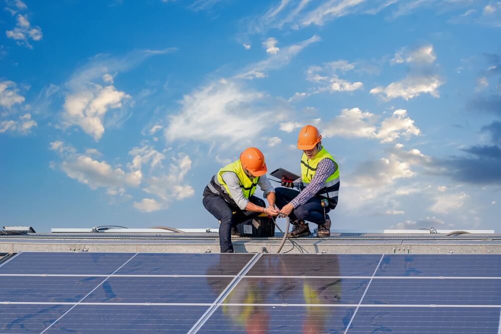 Two engineers wiring rooftop solar panels during a PV system installation.