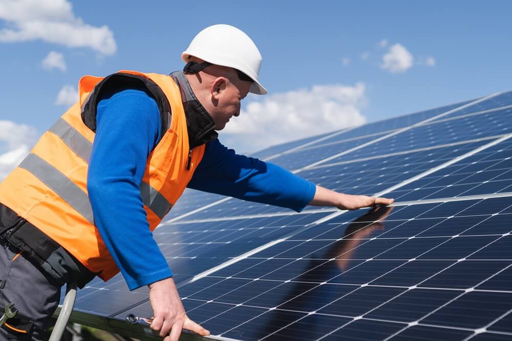 Technician in high-vis inspecting rooftop solar panels on a sunny day.
