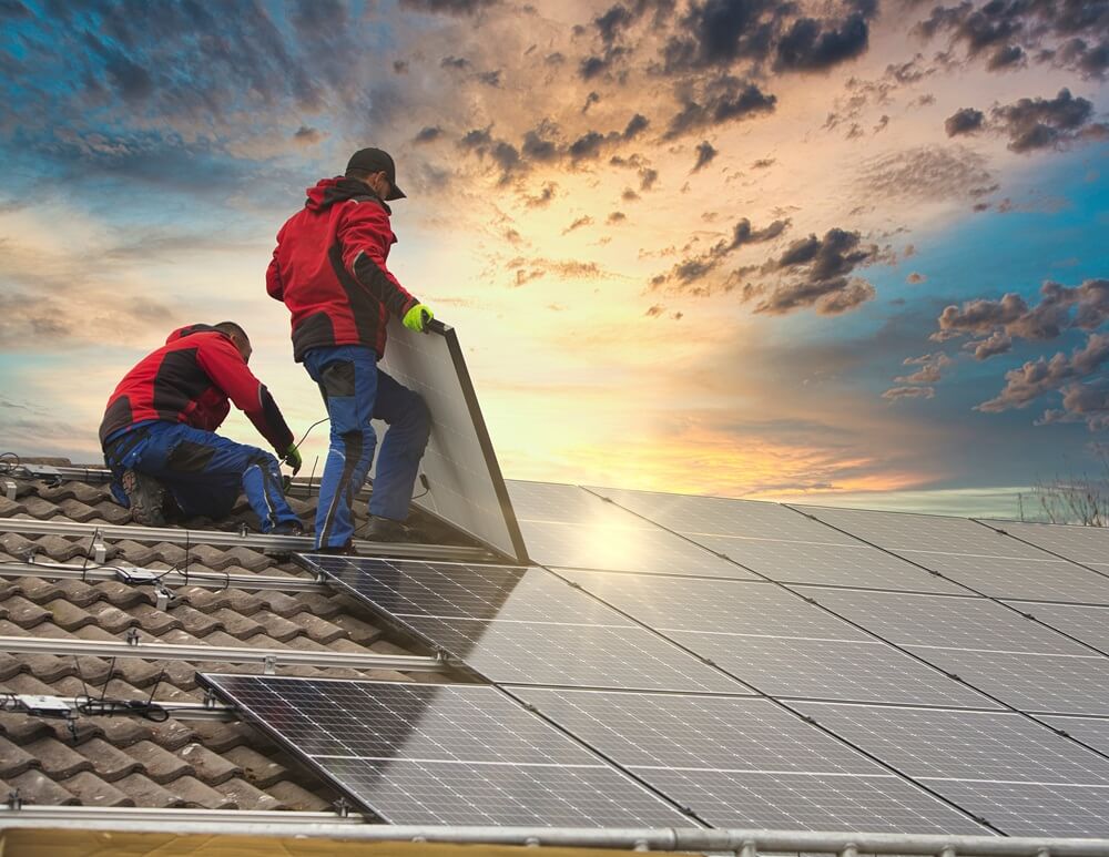 Two solar panel installers fitting rooftop panels during sunset as part of a professional installation.