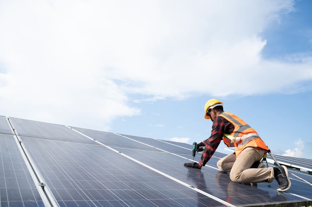 Technician drilling rooftop solar panels during a residential installation under bright skies.