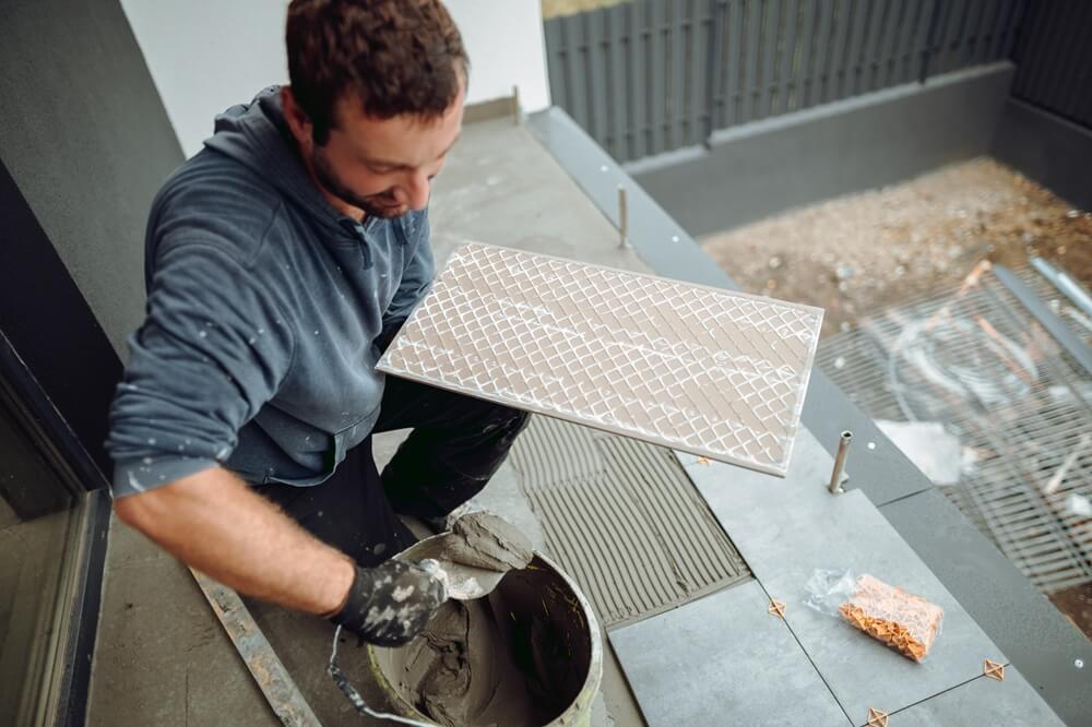 Flooring contractor applying adhesive to the back of a floor tile before fitting.