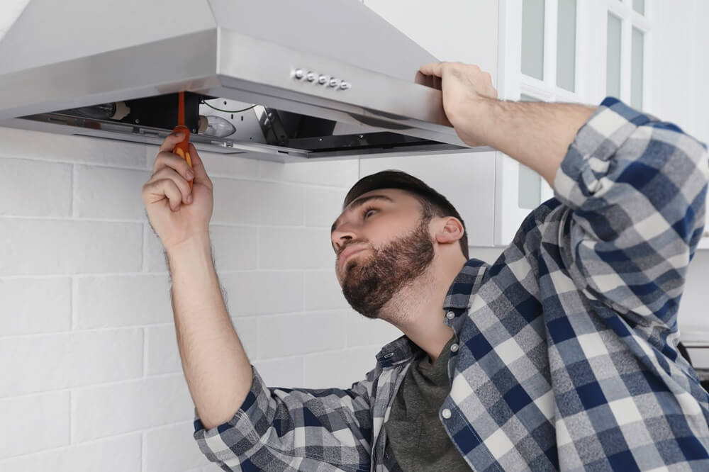 Kitchen fitter securing a cooker hood during installation in a modern kitchen.