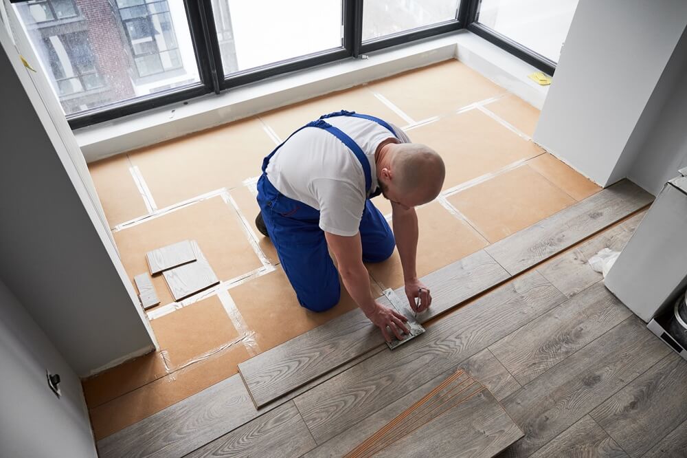 Flooring contractor marking a laminate board with a ruler for accurate cutting during a professional flooring installation.