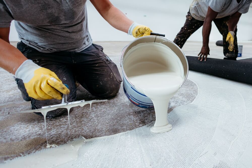 Two flooring contractors spreading adhesive and preparing to lay commercial roll flooring.