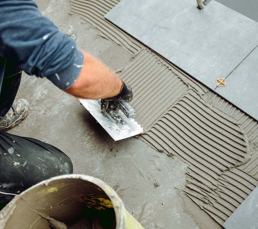 Marketing for tilers showing a professional laying floor tiles with adhesive and trowel, representing skilled craftsmanship and the need for effective tiler marketing services.